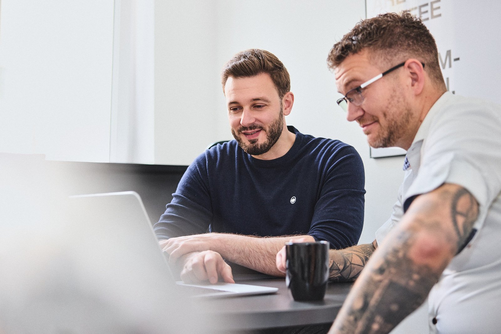 Zwei Kollegen arbeiten gemeinsam am Laptop, Kaffeetasse im Vordergrund
