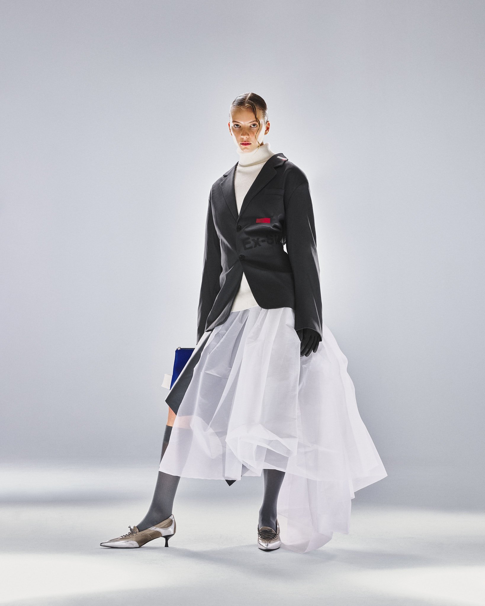 Schwarzer Blazer mit weißem Tüllrock und blauer Clutch